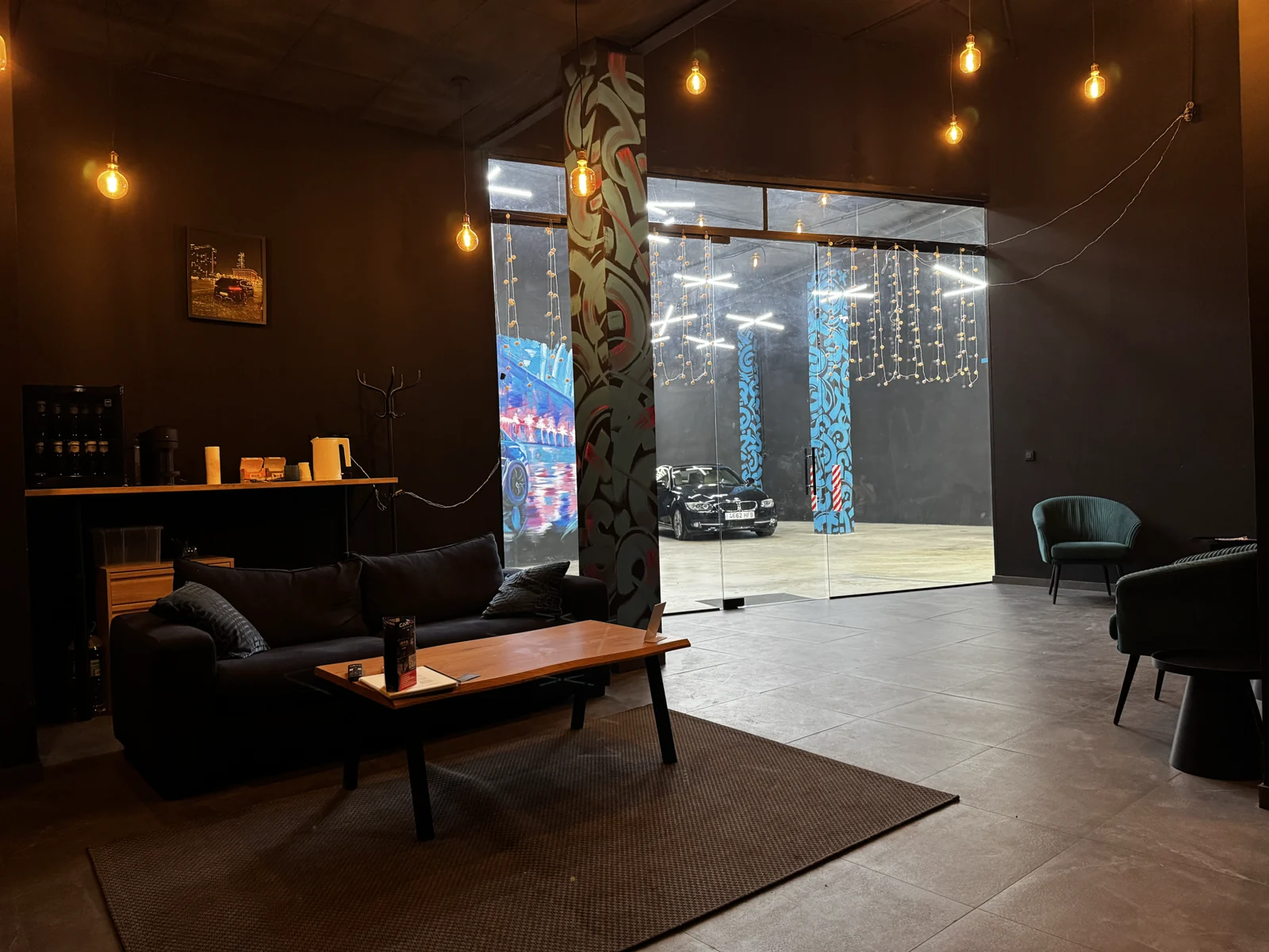 Zona de espera con sofá, sillones y cristalera hacia el taller